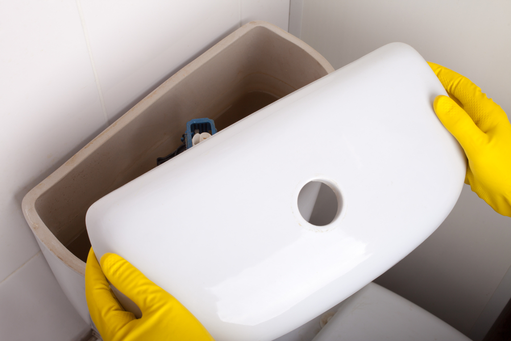 Overhead view of a person wearing rubber gloves removing the lid of a toilet tank.