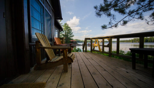 Side view of two chairs on a cottage porch with the lake in the background.