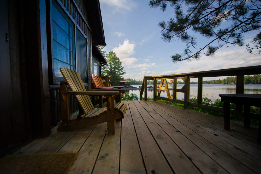 Side view of two chairs on a cottage porch with the lake in the background.