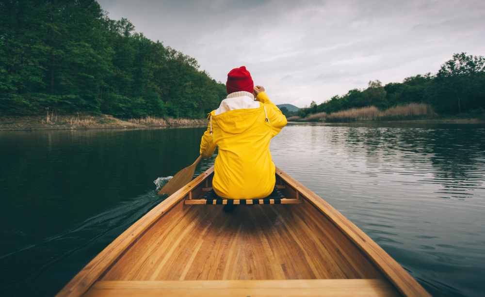 Rear view of a woman in a yellow jacket paddling a canoe.