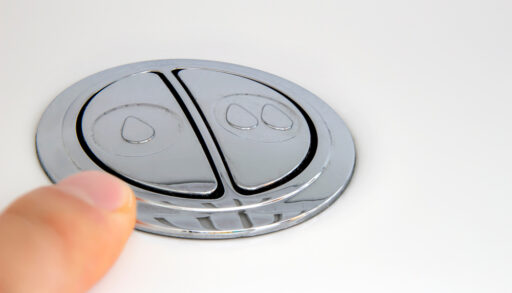 Finger above a low-flow toilet flush button.