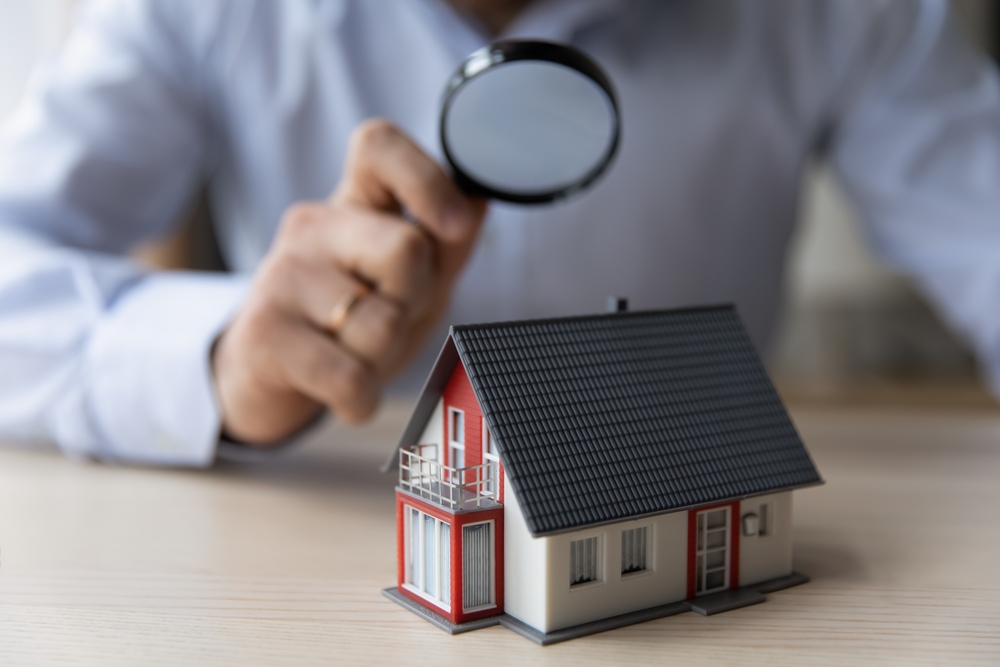 Man holding a magnifying glass looking at a small cottage.