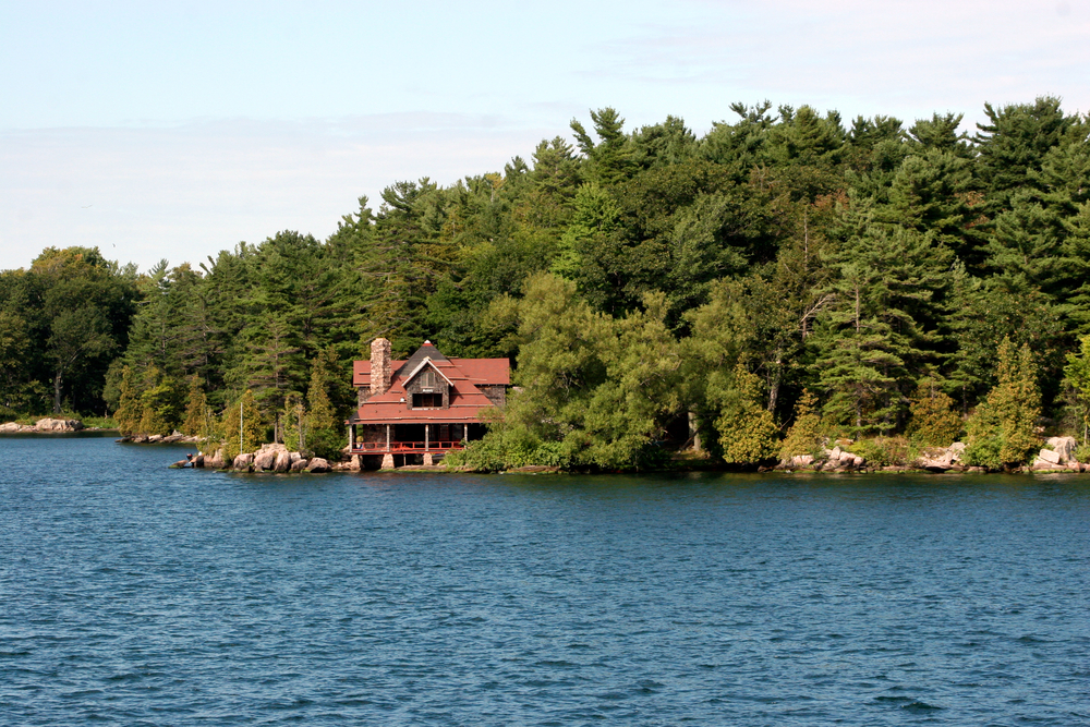 Red waterfront cottage surrounded by green trees.