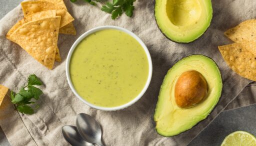 Flat lay of green avocado salsa surrounded by a whole avocado sliced in half and tortilla chips.