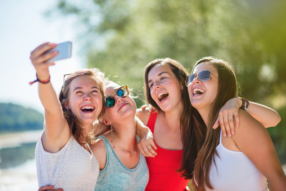 Four teenage girls taking a photo by a lake together.