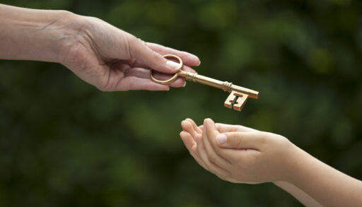 Parent handing down a key to a child with trees in the background.