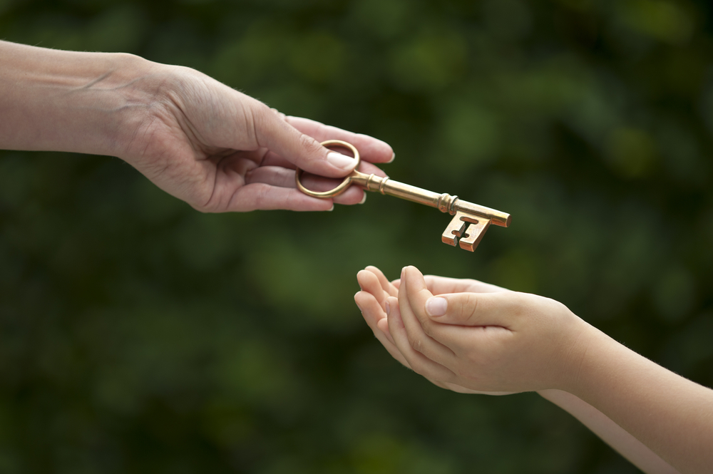 Parent handing down a key to a child with trees in the background.