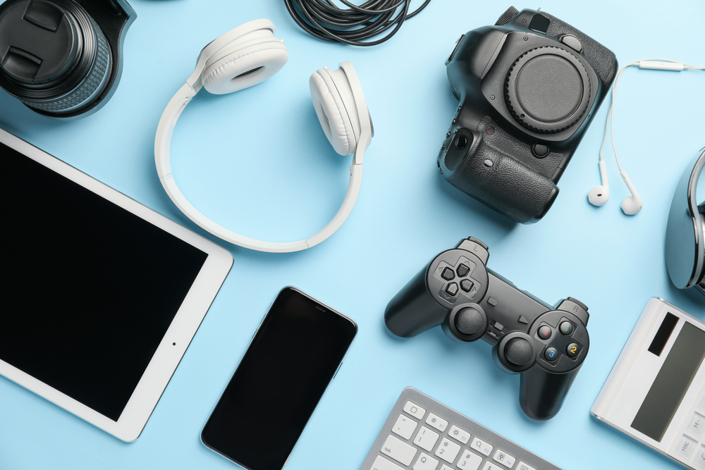 Various electronic devices on a blue background, including game controllers, headphones, smartphones and tablets.