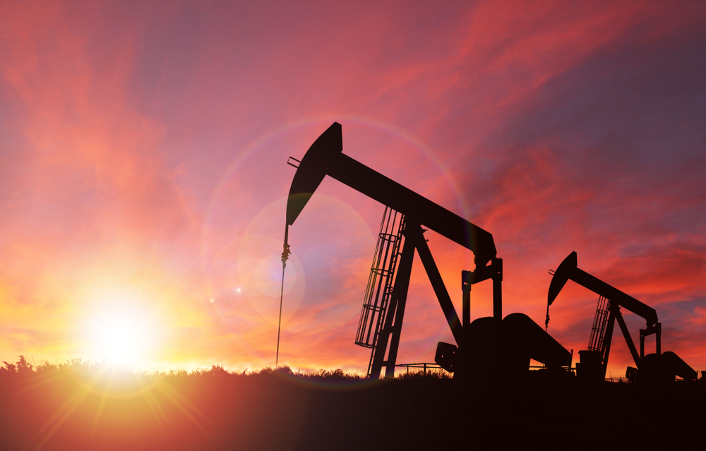 Pumpjack silhouette against a sunset sky with deliberate lens flare