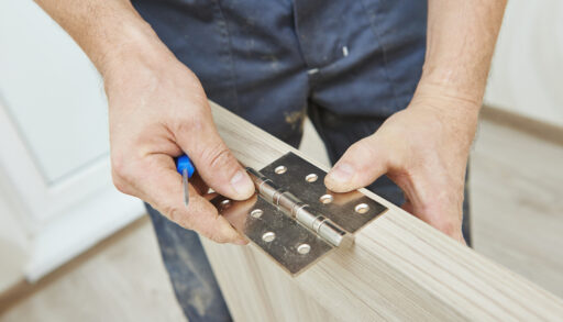 Man putting a metal hinge on a wooden door.