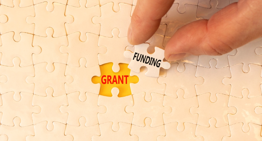 Person placing a puzzle piece with the word "Funding" into a spot reading "Grant."