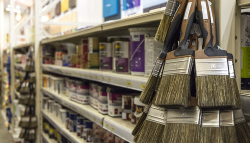 Close-up of paint brushes in front of a shelf of paint cans.