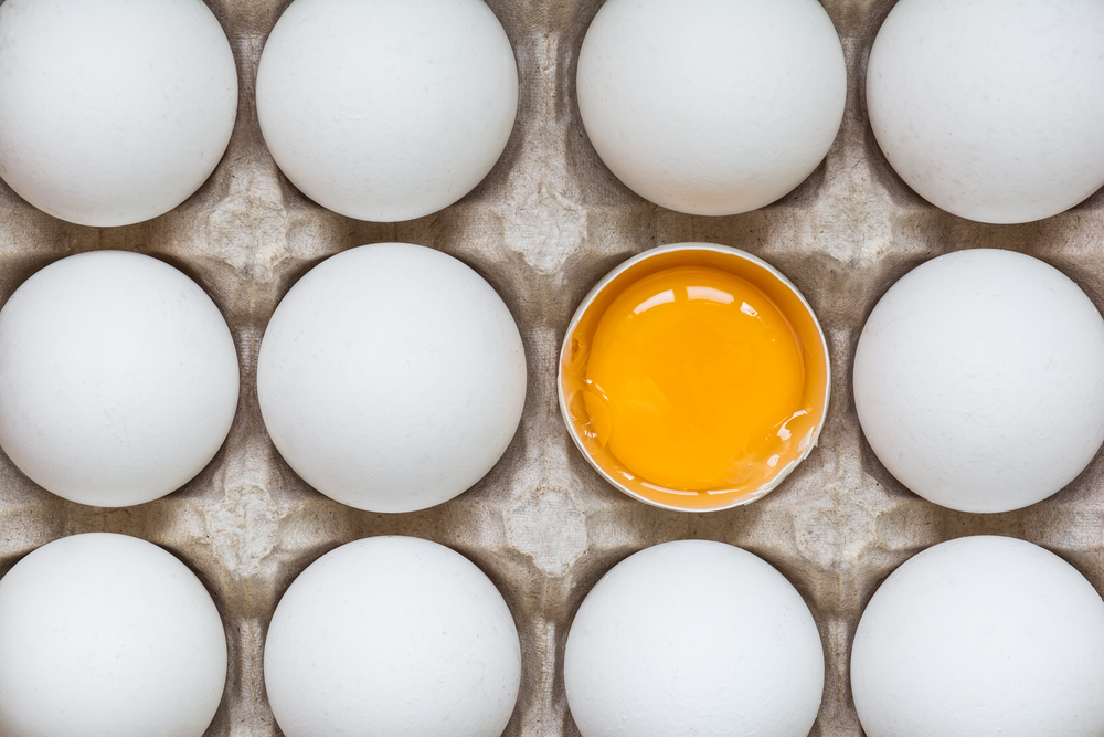 Overhead view of eggs in a carton with one egg cracked in half showing the yolk.
