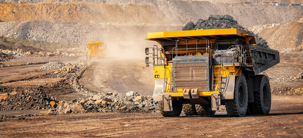 Yellow dump truck carrying sediment out of an open mining pit.