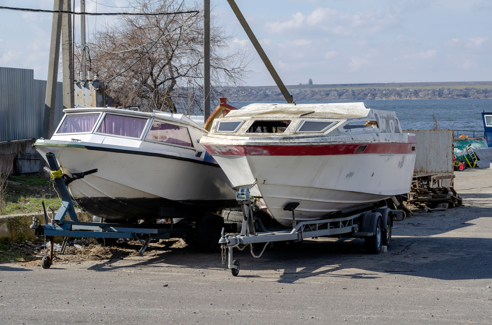 Two used boats parked on the pavement near the water.