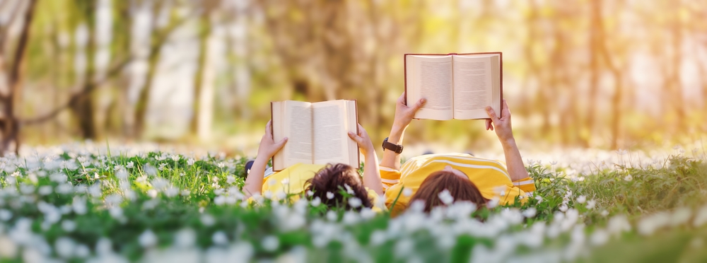 Mother and son laying in a grassy field reading books.