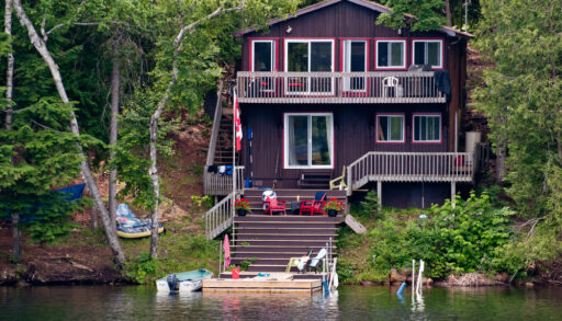 Two-storey brown cottage next to a dock on a lake.