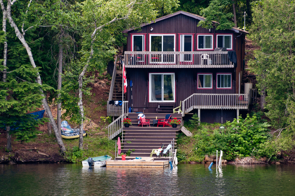Two-storey brown cottage next to a dock on a lake.