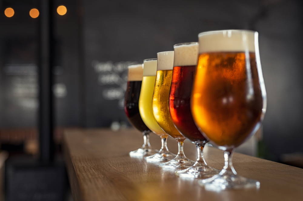 Row of different types of beer in glasses on a wooden countertop.