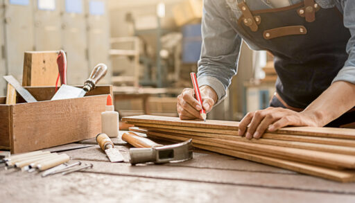 Carpenter measuring wood with a stack of tools on a workbench.