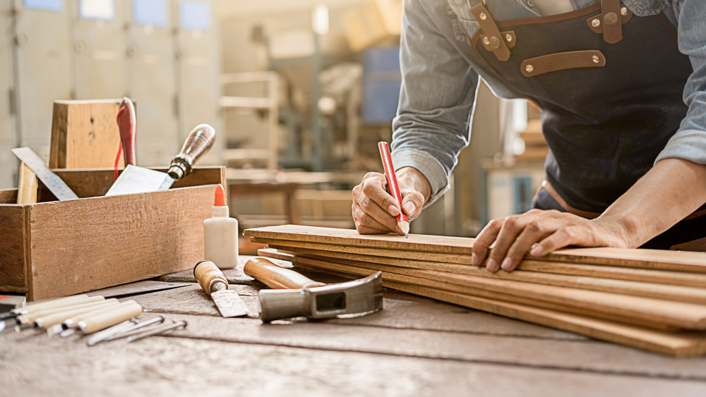 Carpenter measuring wood with a stack of tools on a workbench.