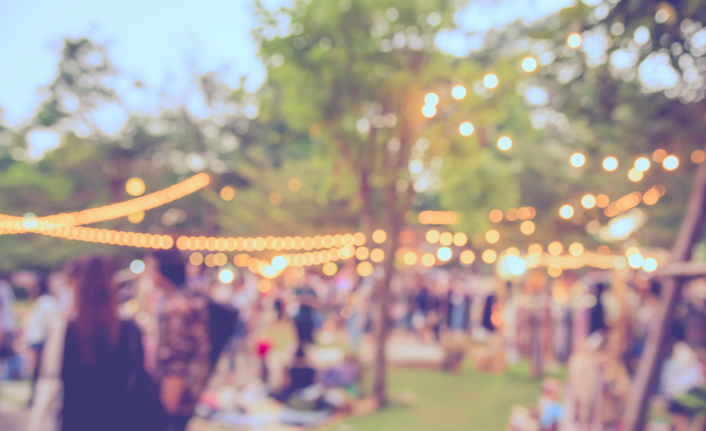 Blurred photo of a summer festival with string lights hung in the trees.