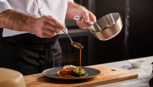 Close-up of a chef pouring a sauce over a plate.