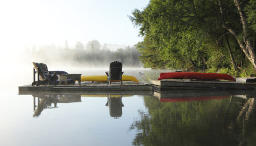 Dock with Muskoka chairs and a canoe on a misty morning in Haliburton, Ontario.