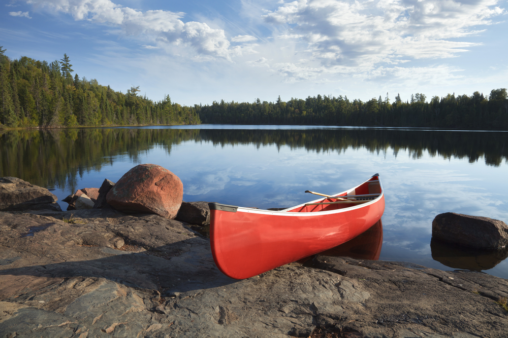 Red canoe on the shore of a lake surrounded by trees.