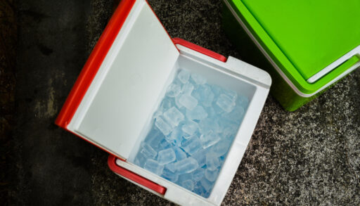Overhead view of an open red cooler with ice cubes inside.