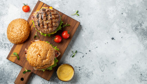 Overhead view of two burgers on a wooden cutting board.