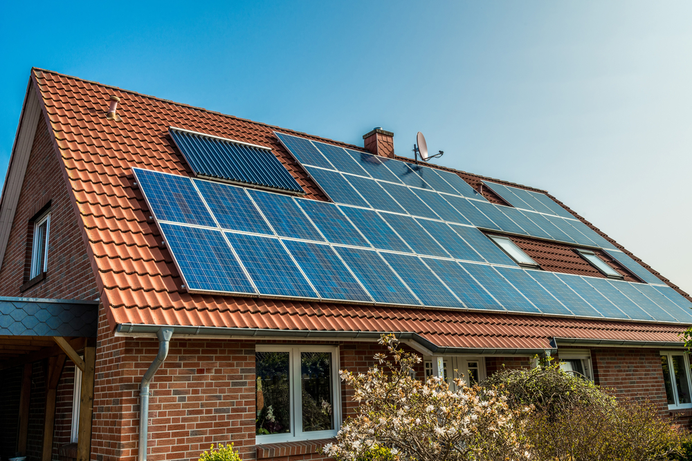 Blue solar panels on top of a red, shingled roof.