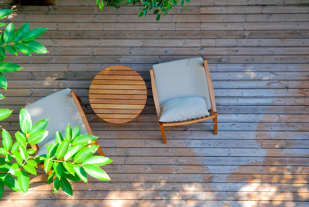Overhead view of a wooden deck with two grey deck chairs next to a green tree.