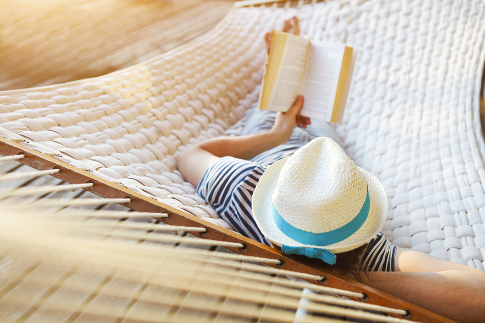 Person laying in a hammock reading a book.