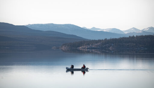 Two people canoeing on a lake surrounded by mountains.