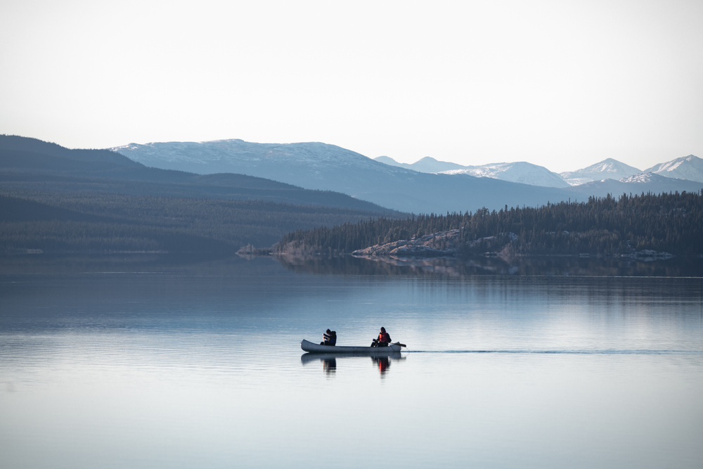 Two people canoeing on a lake surrounded by mountains.