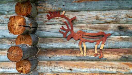 Wooden deer painted red attached to the wall of a log cabin.
