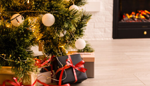 Close-up of presents around a Christmas tree with a fireplace in the background.