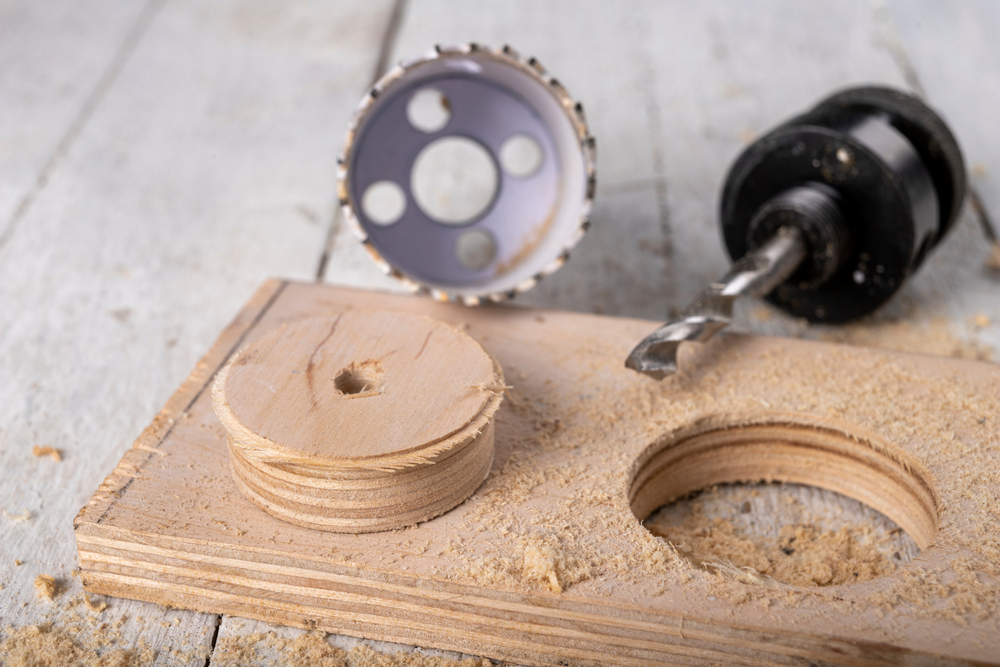 Hole saw next to a piece of wood with a circular cutout.