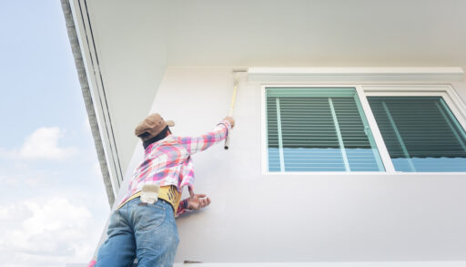 Person painting the side of a white house with an extendable paint pole.