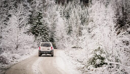 Whistler BC, Canada - Nov 30th, 2023: A four wheel drive, or 4x4 SUV travels down a back road, near Whistler BC, flows through winter forest crusted in ice and snow. Snow covered gravel back road.