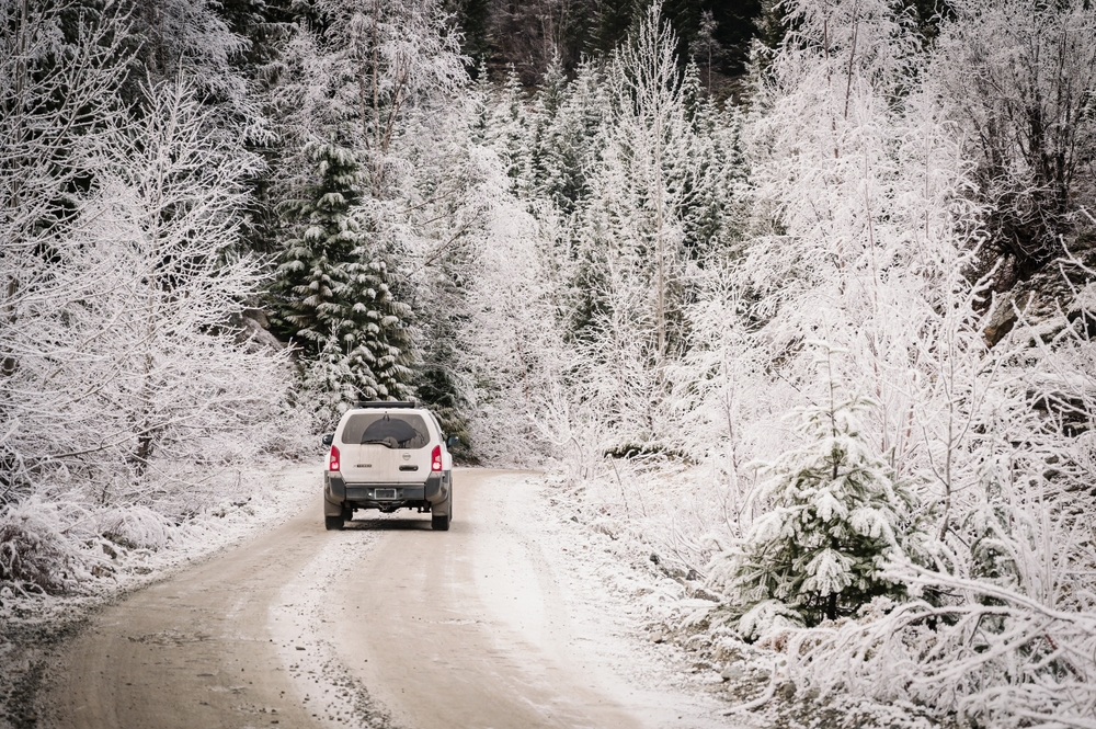 Whistler BC, Canada - Nov 30th, 2023: A four wheel drive, or 4x4 SUV travels down a back road, near Whistler BC, flows through winter forest crusted in ice and snow. Snow covered gravel back road.