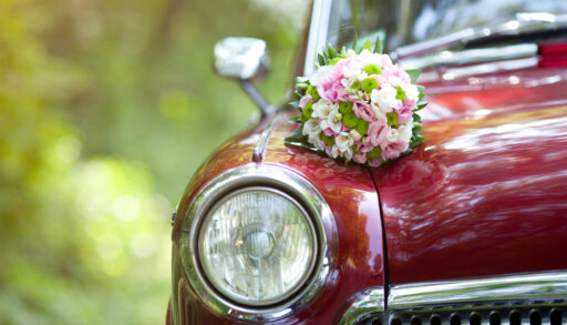 Close-up of a vintage red car with a wedding bouquet on the hood.