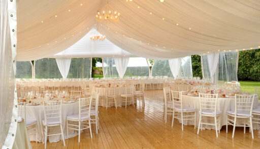 Interior of a wedding tent with white tables and chairs.