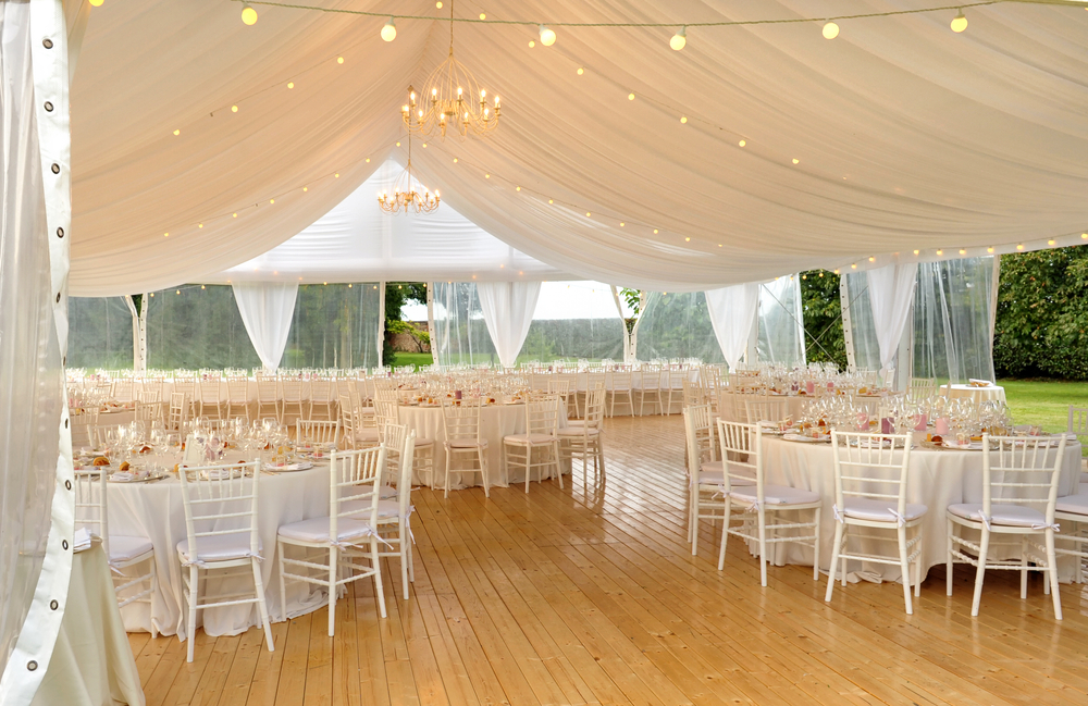 Interior of a wedding tent with white tables and chairs.