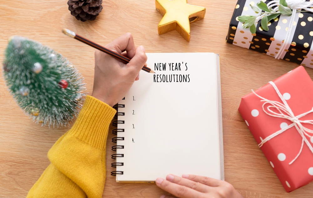 Overhead view of a person writing on a notepad with holiday decorations on the table.