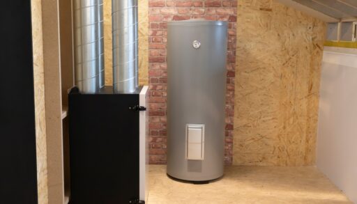 Grey water heater in an unfinished room with plywood and brick walls.