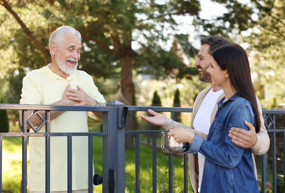 Young man and woman talking with an older man next to a fence.