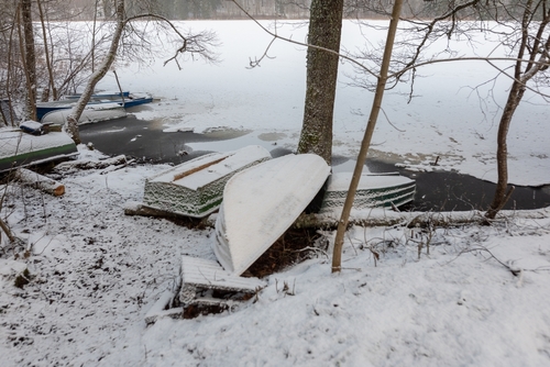Flipped over boat covered in snow on a snowy shore.