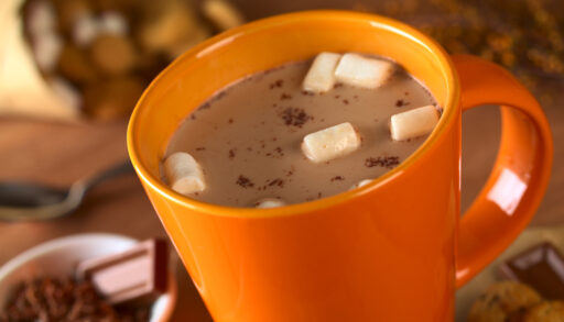 Hot chocolate with marshmallows in orange cup surrounded by chocolate and cookies